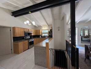 A modern kitchen with wooden cabinets, a central island, and a black railing. - Spacious Ranch on Large Lot W Ample Parking (Wichita)