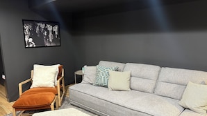 A modern living room with a grey sofa, a wooden chair, and a small side table. - Spacious Ranch on Large Lot W Ample Parking (Wichita)