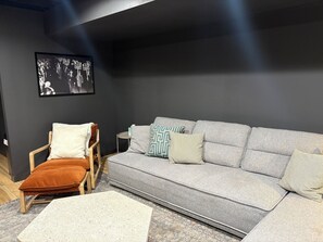 Ein modernes Wohnzimmer mit einem grauen Sofa, einem Holzstuhl und einem kleinen Beistelltisch.