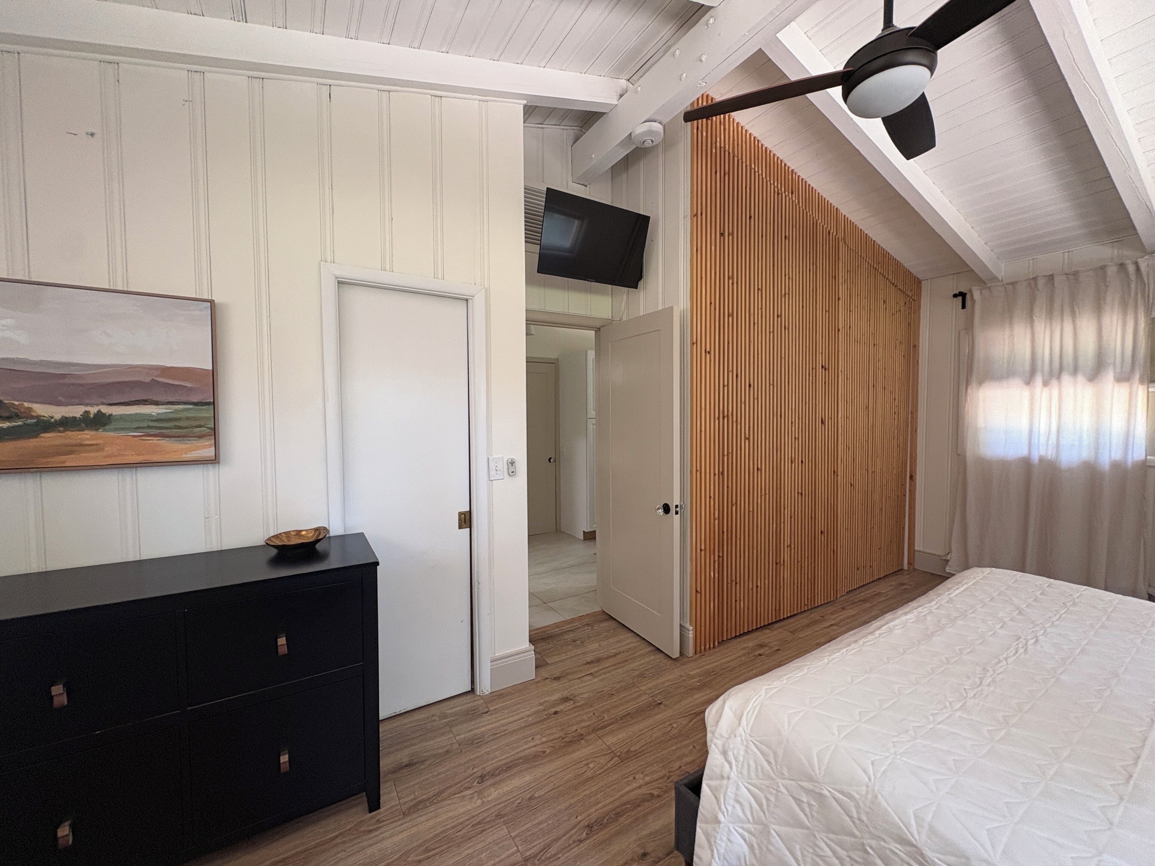 A bedroom with a bed, a dresser, a painting, and a sliding door leading to another room.