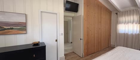 Un dormitorio con cama, cómoda, un cuadro y una puerta corredera que da a otra habitación.