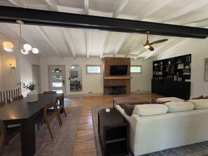 Ein geräumiges Wohnzimmer mit Kamin, einem Essbereich mit Tisch und Stühlen, einer Couch und einem Bücherregal.