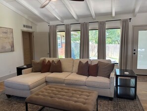 Ein Wohnzimmer mit einem Ecksofa, einem Hocker und einem Beistelltisch.