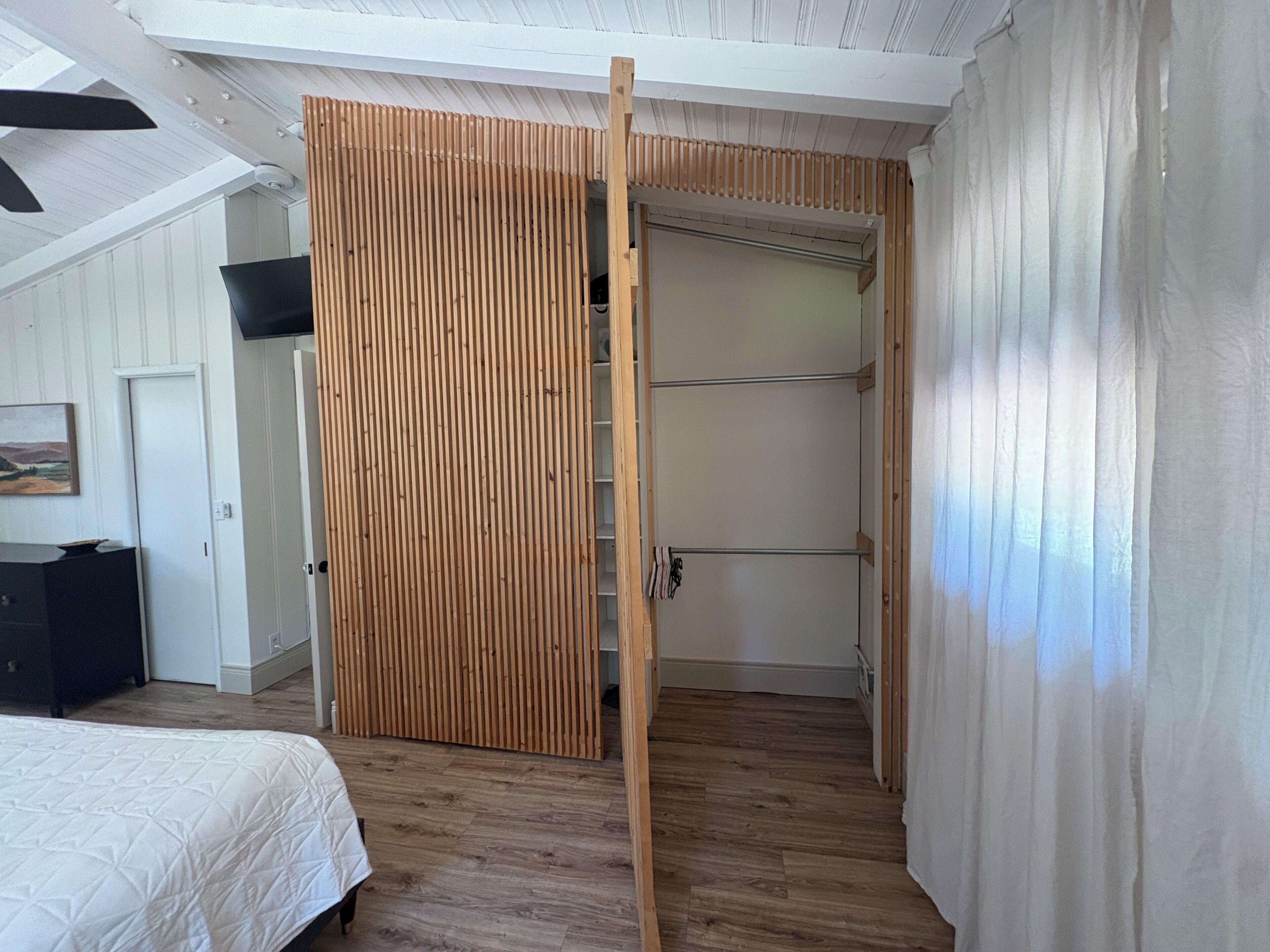 A bedroom with a wooden wardrobe, a bed with a white duvet, and a ceiling fan.