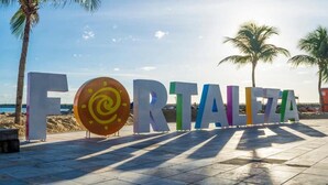 A beachside sign with the word 'FORTALEZA' in large letters, with a palm tree and a clear sky in the background. - Hostel Way Fortaleza (Fortaleza)