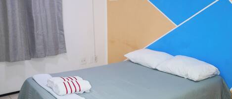 A single bed with a blue bedspread, a white pillow, and two towels.