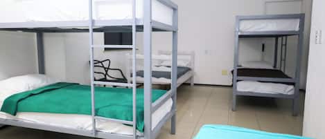 A dormitory room with bunk beds, a green blanket, and a blue towel on the floor.