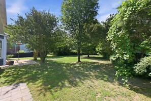 Un giardino sul retro di una casa con prato, alberi e canestro da basket.