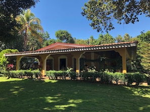A covered outdoor area with a red roof, surrounded by lush greenery and trees.