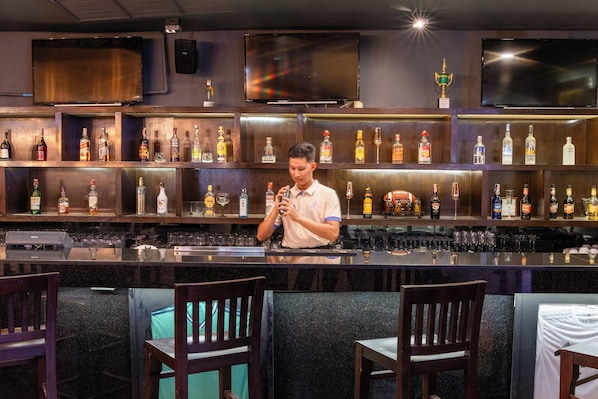 A bar area with multiple shelves of liquor bottles, a bartender preparing drinks, and bar stools.