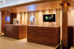 A reception area with wooden reception desks and a digital screen displaying the Holiday Inn Phuket Resort name. - Holiday Inn Resort Phuket Surin Beach (Choeng Thale)