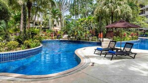 A swimming pool with lounge chairs and umbrellas, surrounded by tropical vegetation.