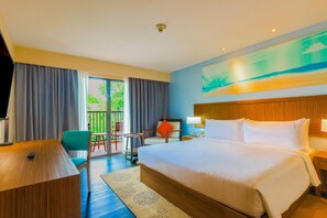 Habitación de hotel con cama, escritorio, silla, mesita y balcón con vistas.