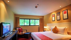 A hotel room with a bed, a desk with a television, a chair, a window with curtains, and a wall with framed pictures.