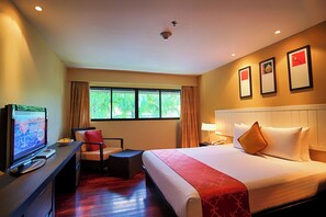 A hotel room with a bed, a desk with a television, a chair, a window with curtains, and a wall with framed pictures.