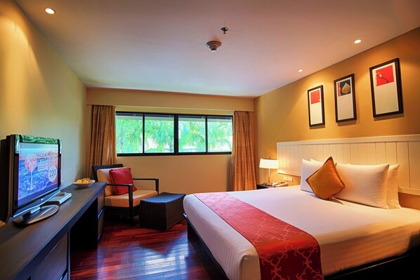 A hotel room with a bed, a desk with a television, a chair, a window with curtains, and a wall with framed pictures. - Holiday Inn Resort Phuket Surin Beach (Choeng Thale)