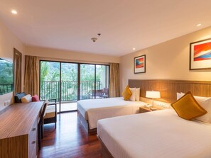 A hotel room with two beds, a desk, a chair, and a balcony with a view of greenery. - Holiday Inn Resort Phuket Surin Beach (Choeng Thale)
