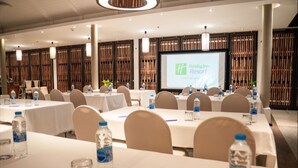 A conference room with multiple tables, chairs, and a large screen displaying the Holiday Inn Resort logo.