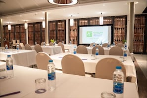 A conference room with multiple tables, chairs, and a large screen displaying the Holiday Inn Resort logo.