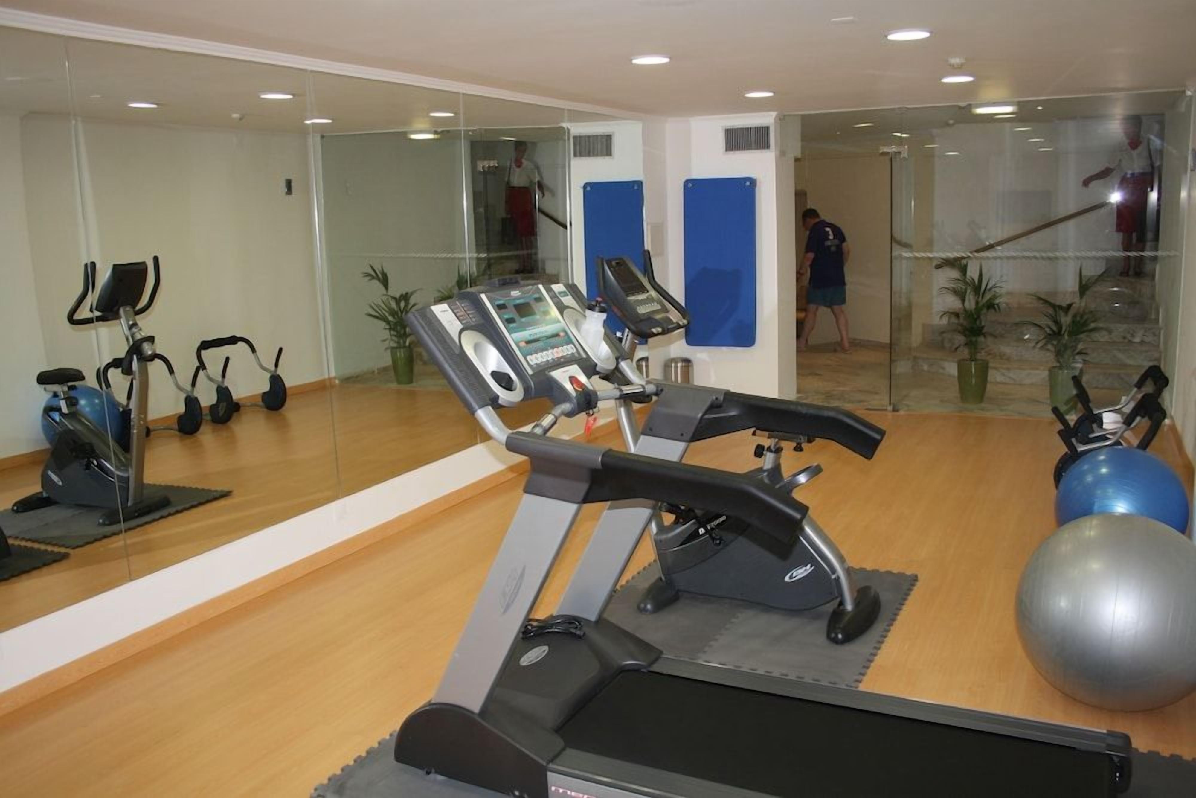 Una sala de gimnàstica amb equip d'exercici, un mirall i una escala.