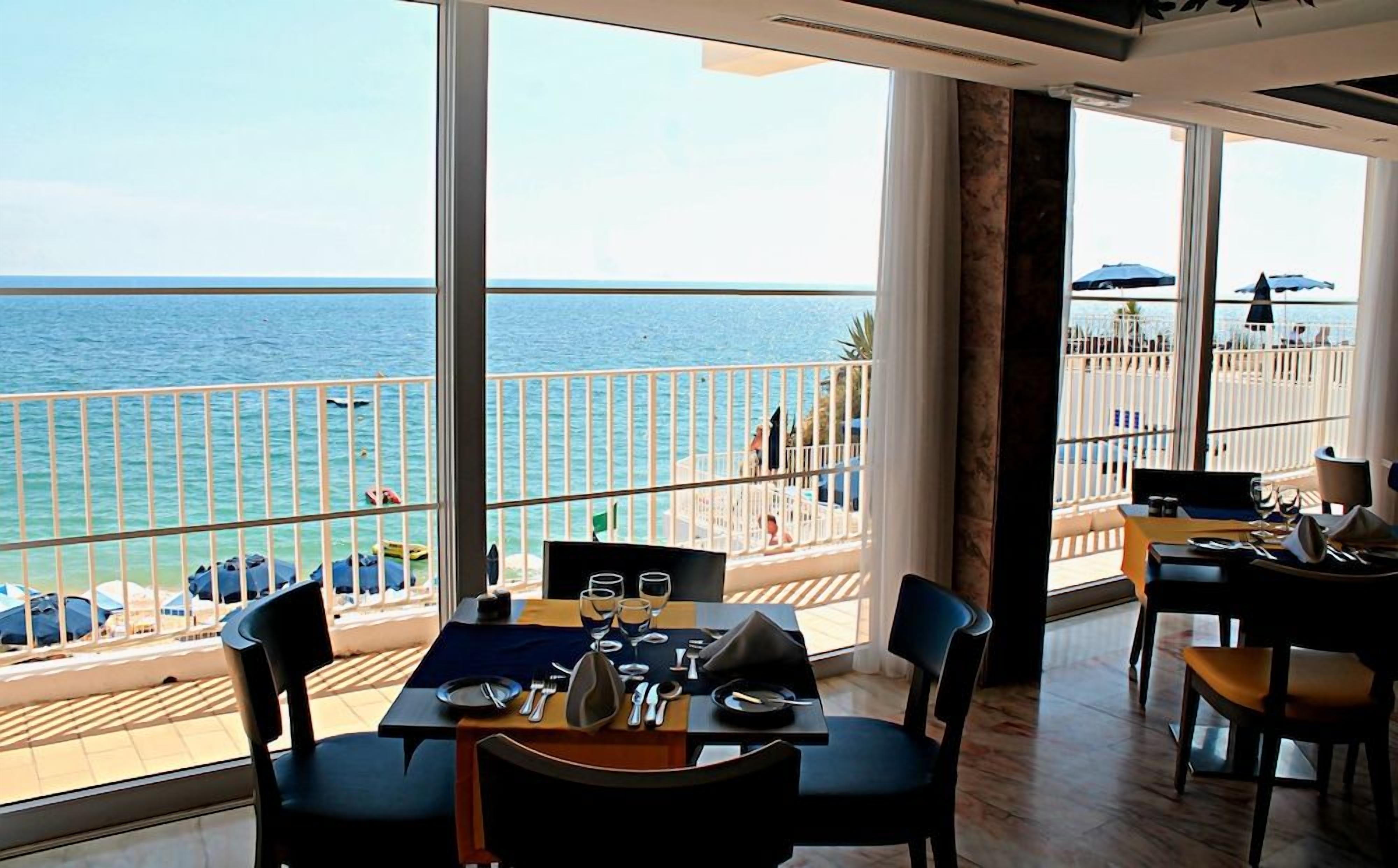 A dining area with a view of the sea, a balcony with a railing, and outdoor seating with umbrellas.
