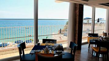 A dining area with a view of the sea, a balcony with a railing, and outdoor seating with umbrellas.