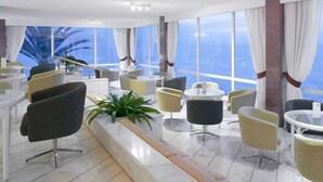 Een moderne hotel lobby met meerdere zithoeken, grote ramen en uitzicht op de oceaan.