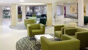 Een hal met groene fauteuils, een witte tafel en een rond tapijt met een patroon.