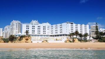 A beachfront hotel with multiple floors, balconies, and a sandy beach in the foreground.