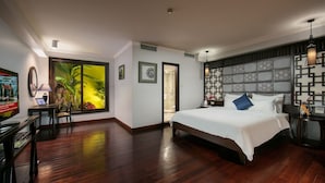 A hotel room with a large bed, a desk with a computer, a TV, and a view of a tropical garden. - Grand Minerva Hotel (Hanoi)