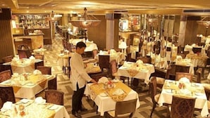 A restaurant with multiple tables set for dining, a waiter attending to guests, and a patterned floor. - Grand Minerva Hotel (Hanoi)