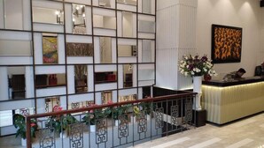 A hotel lobby with a reception desk, a decorative wall with mirrors, and a staircase with railings. - Grand Minerva Hotel (Hanoi)