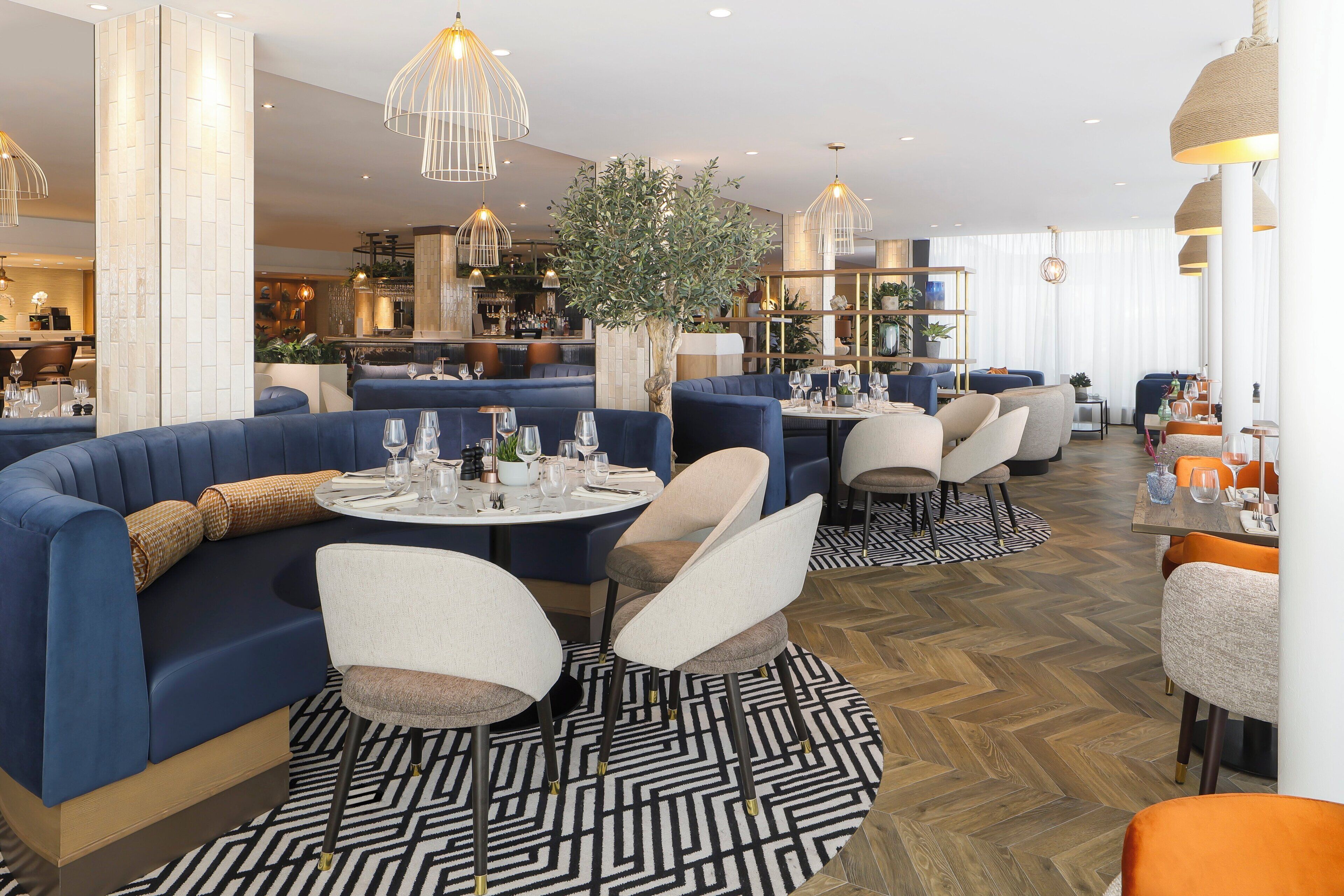 A modern restaurant with round tables, blue seating, and a herringbone wood floor.