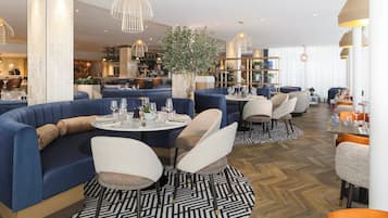 A modern restaurant with round tables, blue seating, and a herringbone wood floor.
