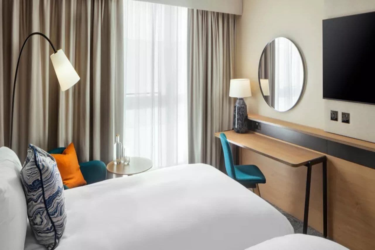 A hotel room with a bed, a desk, a chair, a round mirror, and a television.