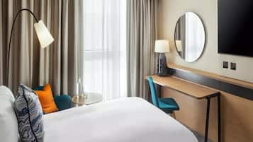 A hotel room with a bed, a desk, a chair, a round mirror, and a television.