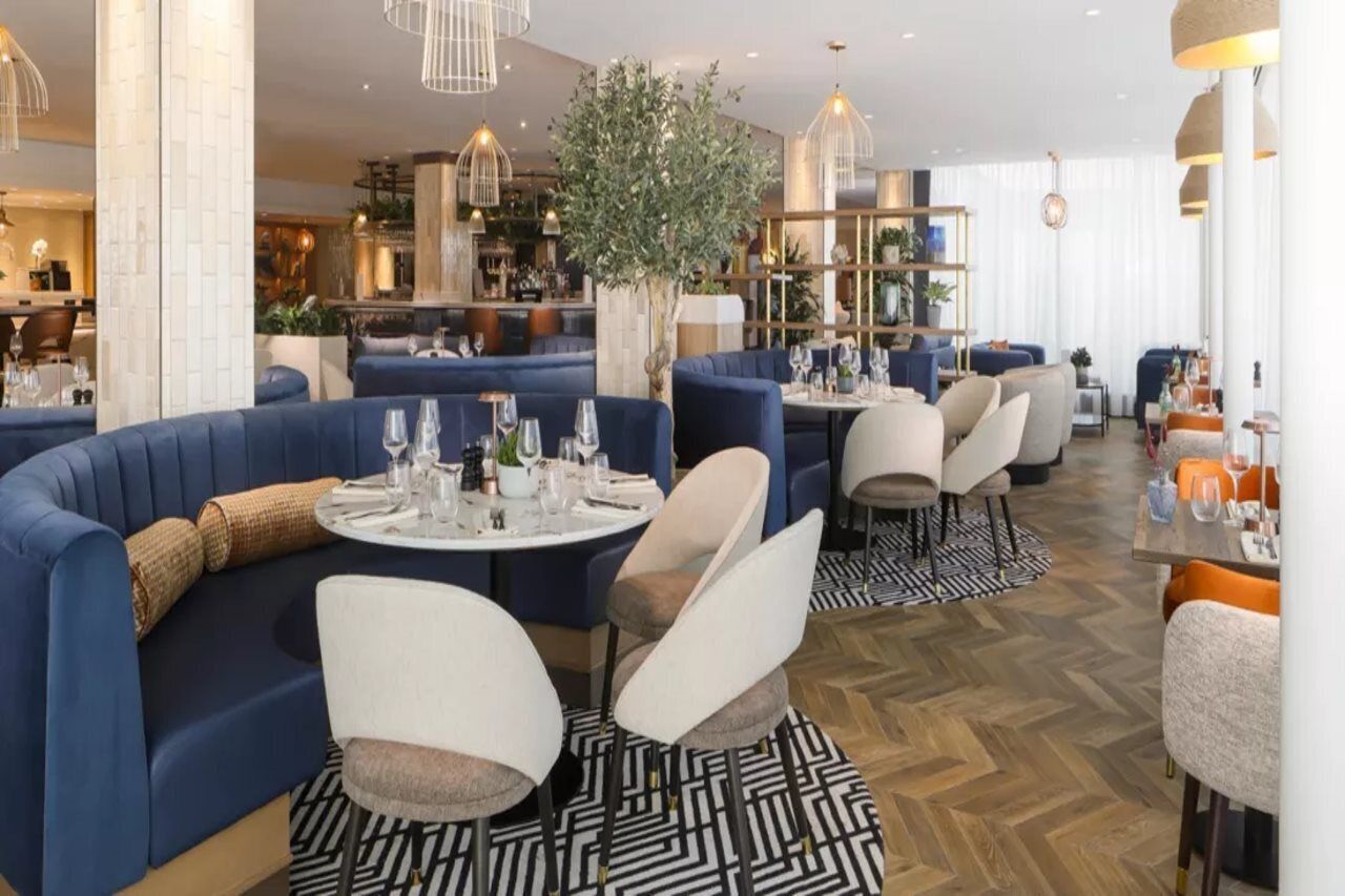 Un restaurante moderno con asientos tapizados en azul, mesas redondas e iluminación contemporánea.