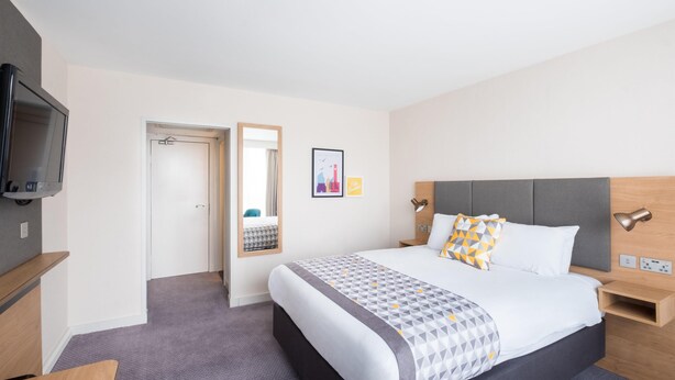 A hotel room with a bed, bedside tables, a TV, a mirror, and a picture on the wall. - Voco Southampton (Southampton)