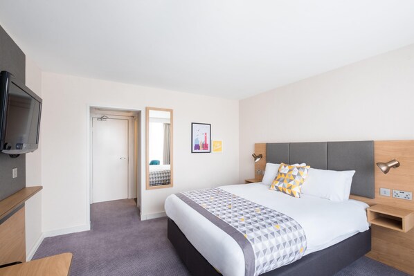 A hotel room with a bed, bedside tables, a TV, a mirror, and a picture on the wall.