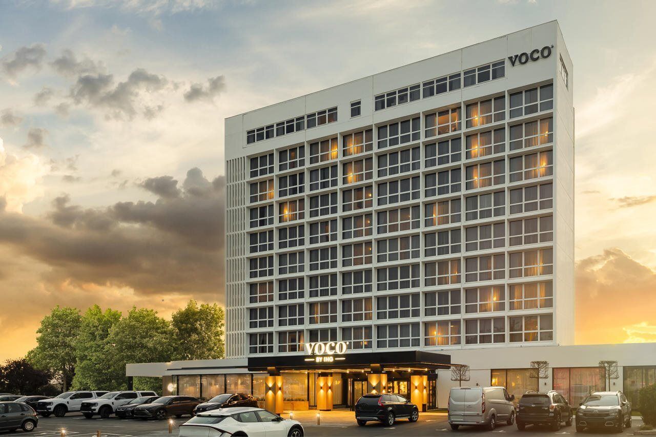 A modern hotel building with a grid of windows, a prominent entrance, and a parking lot.