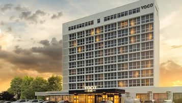 A modern hotel building with a grid of windows, a prominent entrance, and a parking lot.
