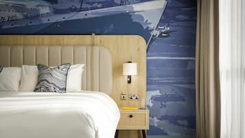 Habitación de hotel con una cama grande, cabecera de madera, mesita de noche con lámpara y un mural en la pared.