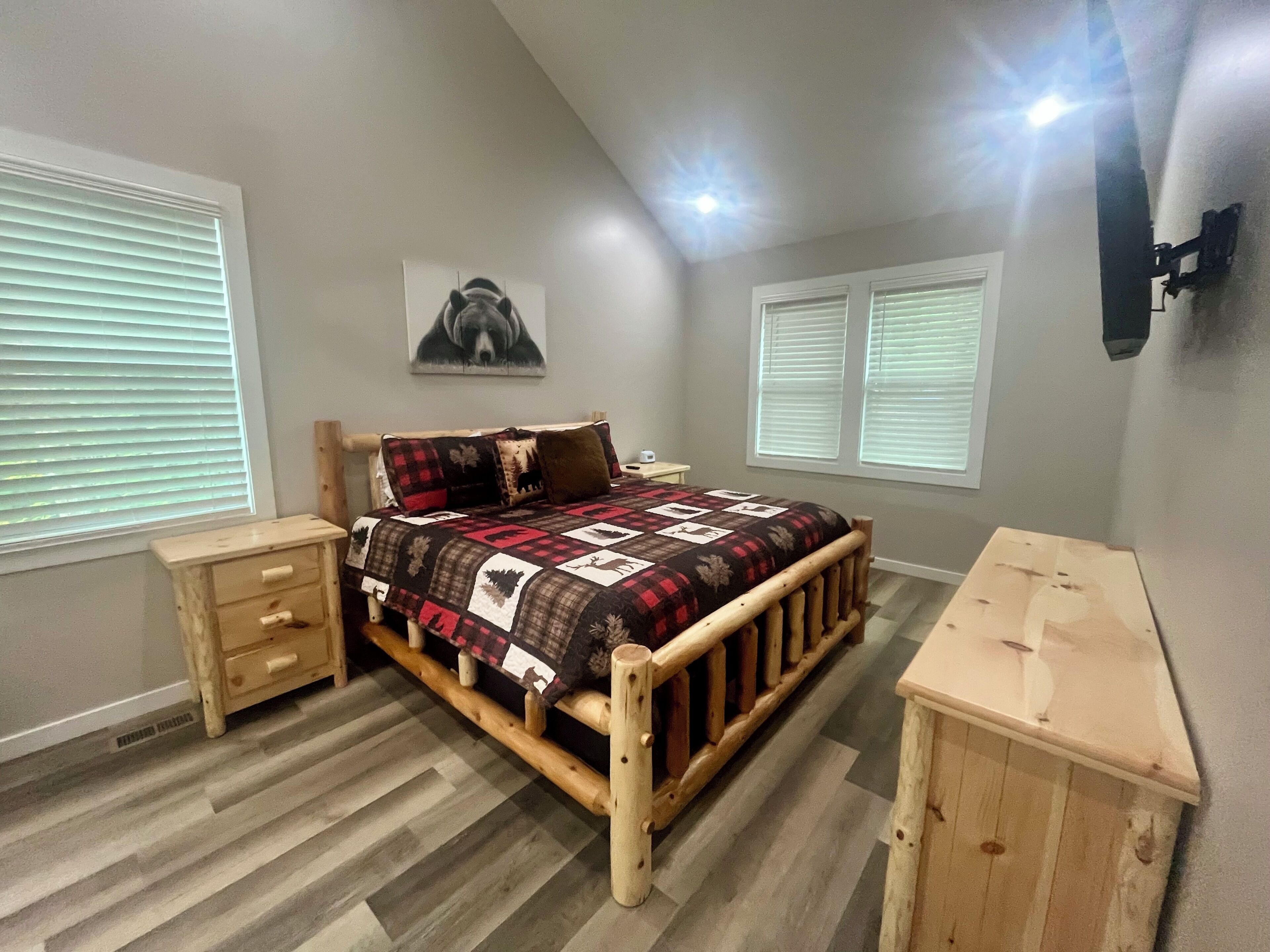 A bedroom with a wooden bed, a nightstand, a dresser, and a wall-mounted lamp.