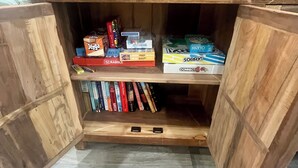 A wooden cabinet with open doors revealing shelves stocked with board games and books. - 3-bedroom cabin close to Downtown Clayton with a Mountain feel. (Clayton)