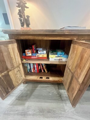 Ein Holzkabinent mit geöffneten Türen, dahinter Regale voller Brettspiele und Bücher.
