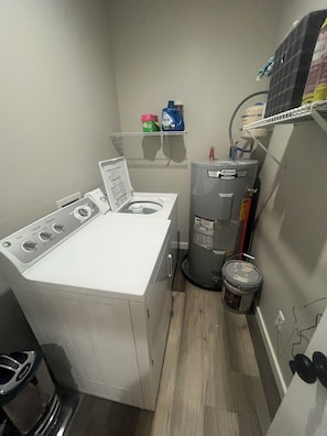 Ein kleiner Hauswirtschaftsraum mit einer Waschmaschine und einem Trockner mit Frontlader, einem Warmwasserbereiter und einer kleinen Ablage für Reinigungsmittel.