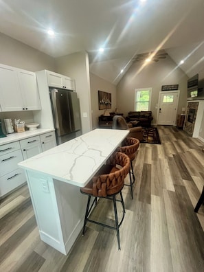 A modern kitchen with a central island, bar stools, and a dining area with a sofa.