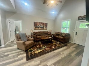 A living room with a ceiling fan, a large rug, and a wall-mounted painting.