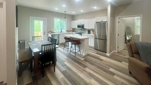 A modern kitchen with white cabinets, a stainless steel refrigerator, and a dining area with a table and chairs. - 3-bedroom cabin close to Downtown Clayton with a Mountain feel. (Clayton)