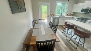 A modern kitchen with white cabinets, a stainless steel microwave, and a wooden dining table with chairs. - 3-bedroom cabin close to Downtown Clayton with a Mountain feel. (Clayton)